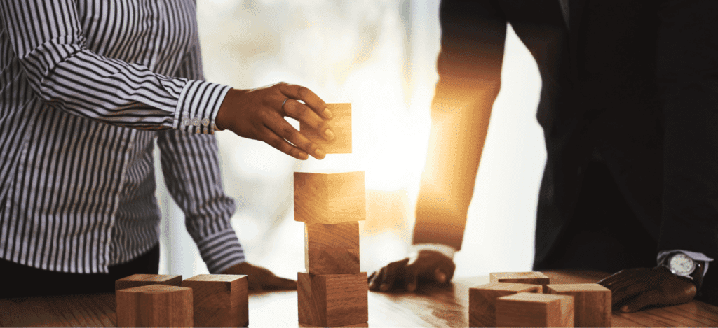 Two individuals stacking wooden blocks, symbolizing building a foundation for growth in healthcare practices.